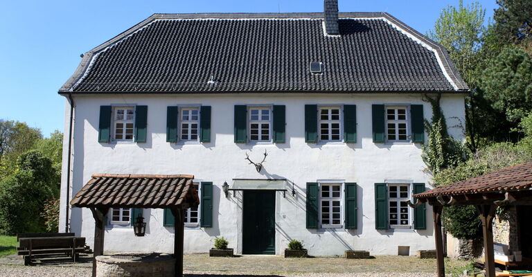 Das historische Gebäude des Forsthauses Steinhaus mit Ziehbrunnen im Vordergrund und Hirschgeweih über der Eingangstür